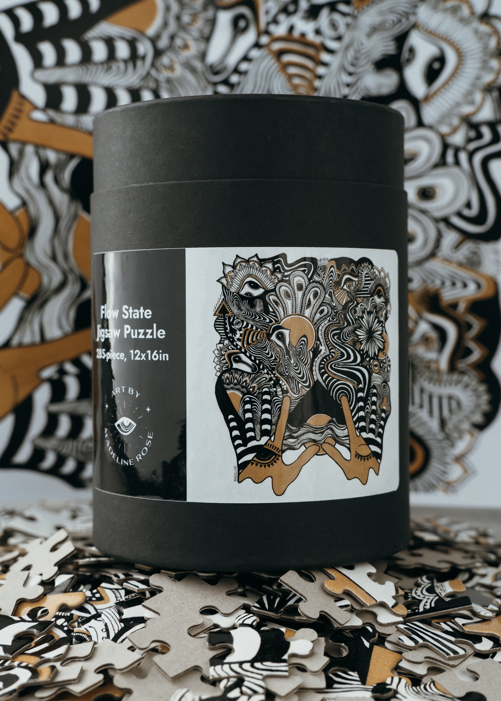 A completed 285-piece jigsaw puzzle with a black lid and a label showing the puzzle image. The background displays a patterned fabric.