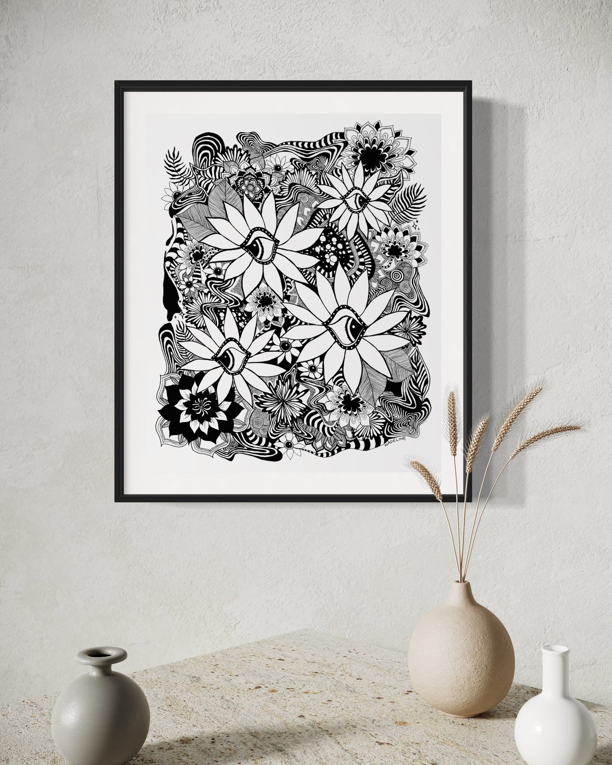 Framed black and white floral artwork on a light gray wall with decorative vases below.