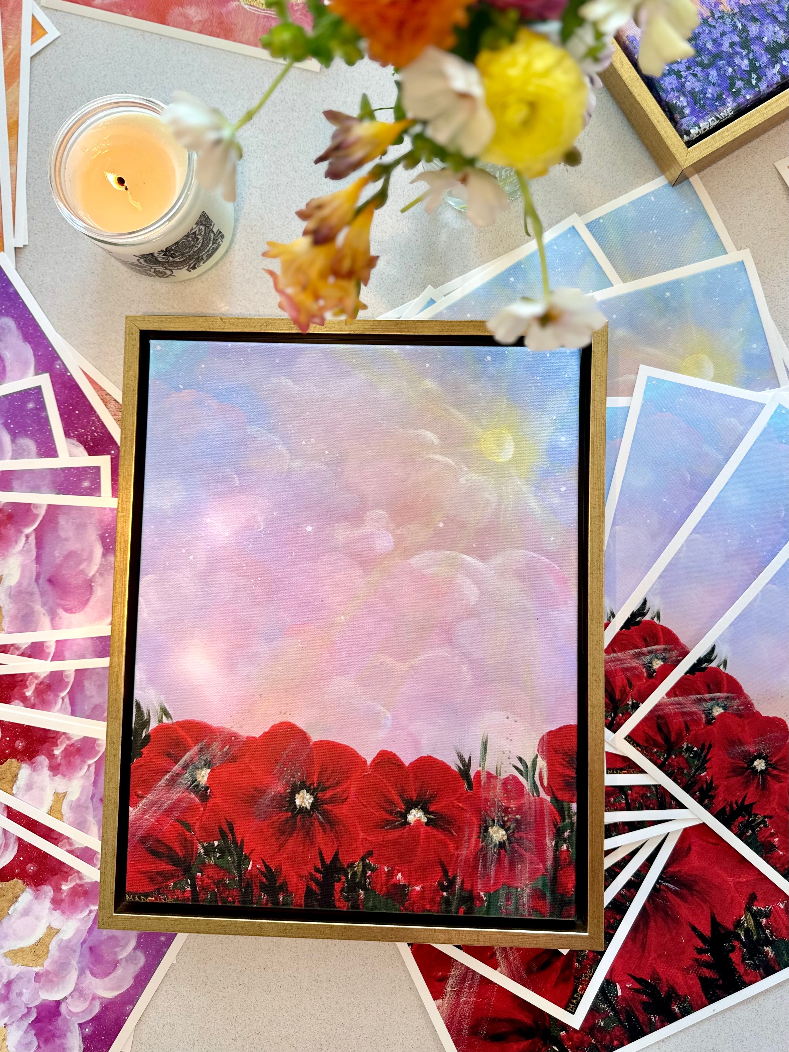 A canvas giclée print featuring a vibrant image of red flowers with a pink and purple gradient sky in the background, displayed on a table with floral patterns and a lit candle.