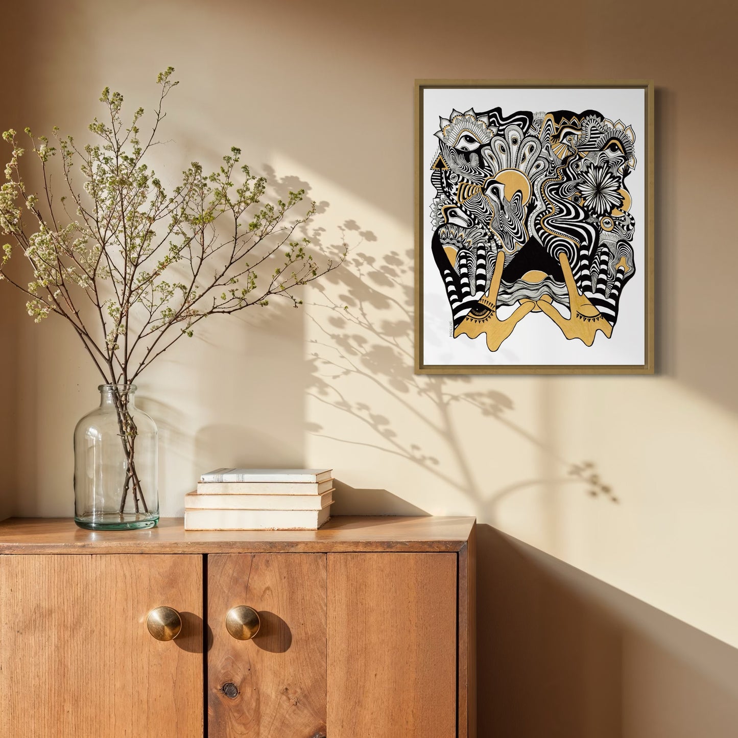 Framed abstract artwork with black, white, and gold designs coming out of two gold hands and fine linework on a white background