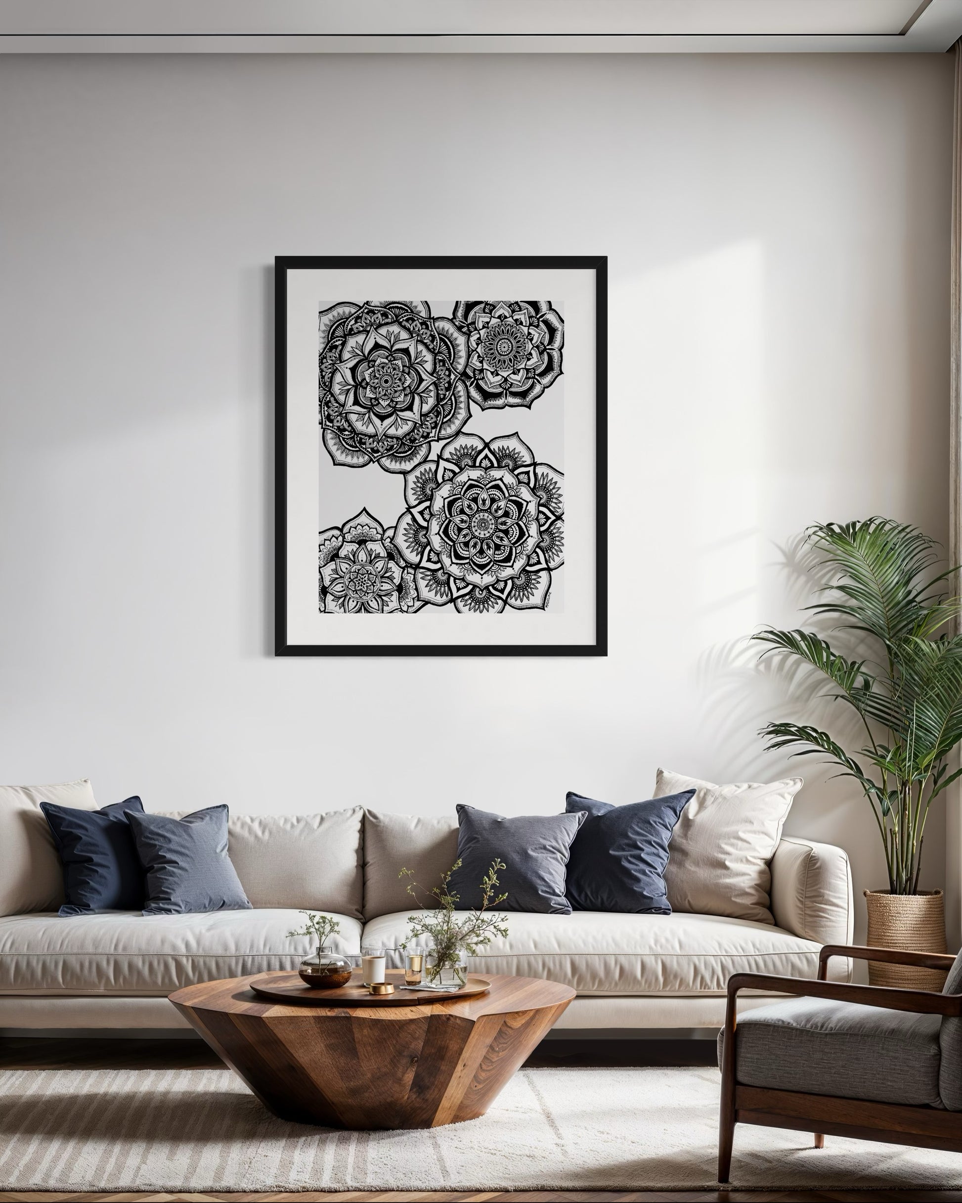 Living room with a white wall, framed black and white floral artwork, beige sofa, wooden coffee table, and potted plant.