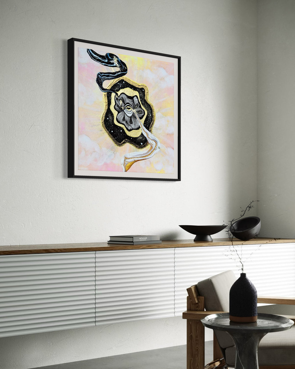 Framed artwork with a black and gold abstract swirls coming out of golden eye on a night sky over a pastel pink and yellow sky background