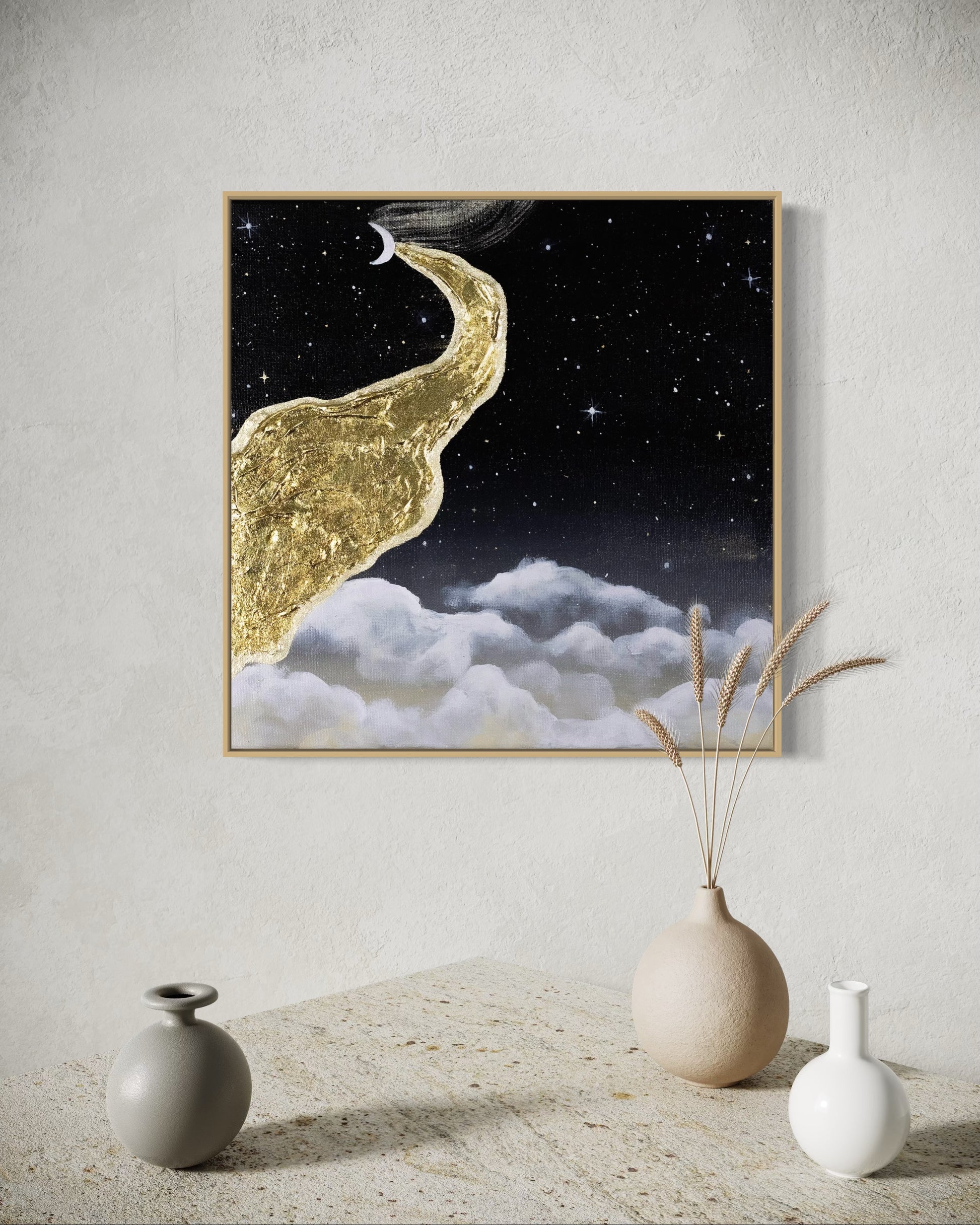 Framed artwork of a gold path leading to a moonlit sky with clouds, displayed on a wall above a table with decorative vases.