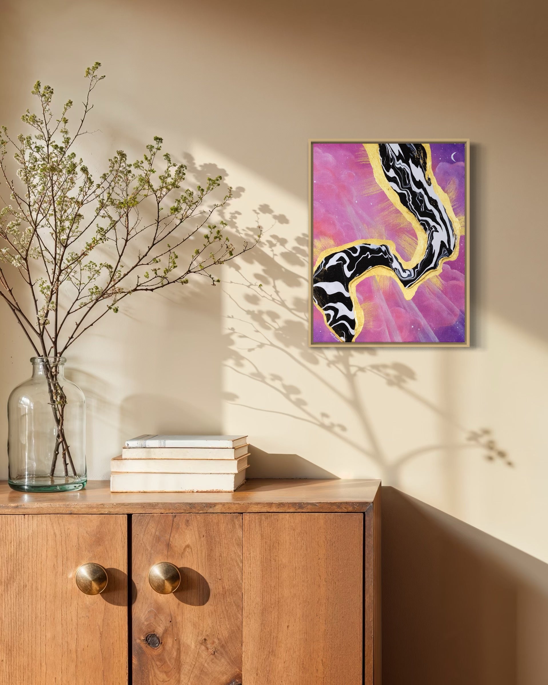 Framed artwork with abstract black and white fluid design on a pink and purple sky background with a moon and gold leaf rays